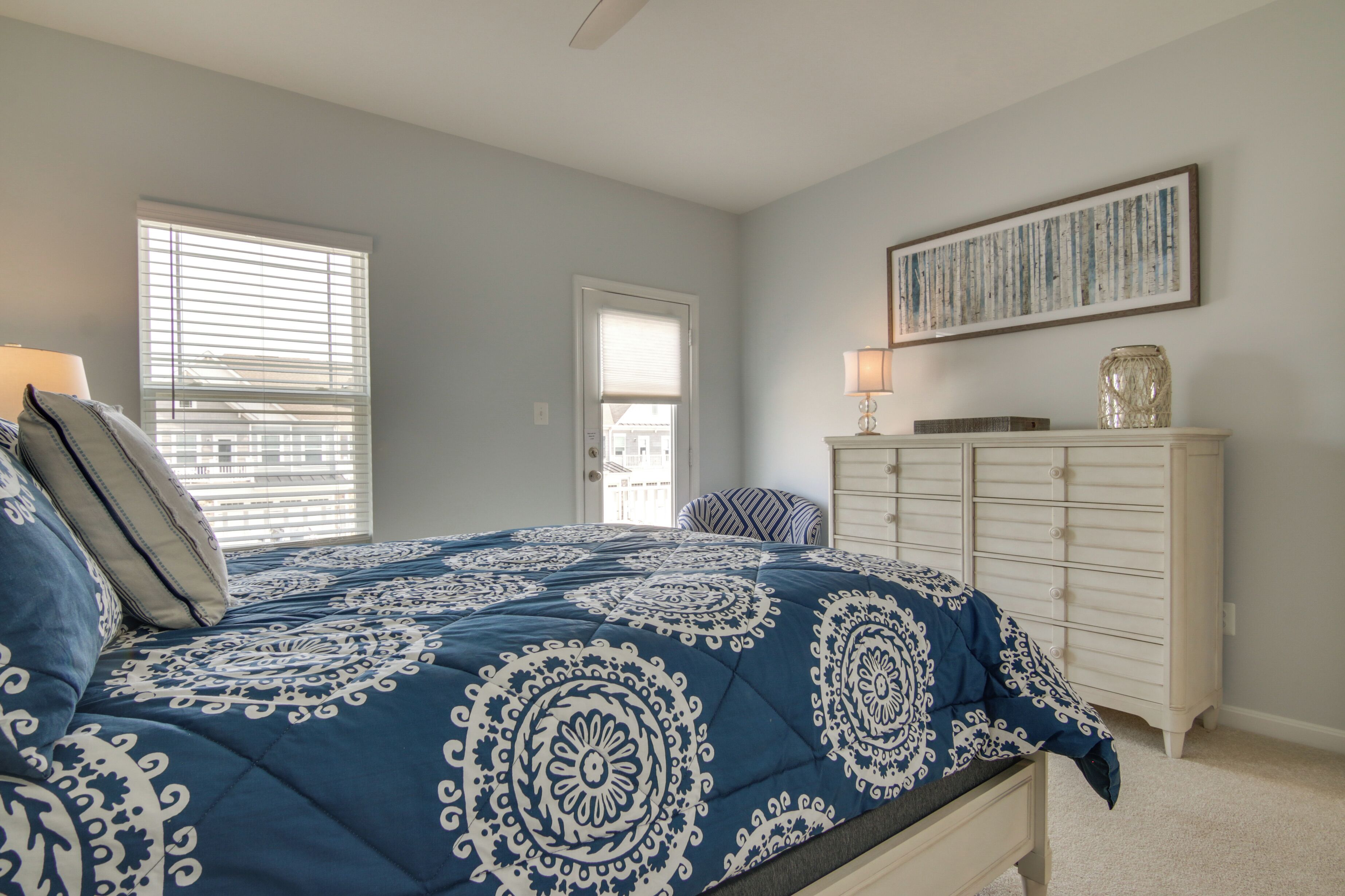 A bedroom with a bed, a dresser, a chair, and a window with blinds.