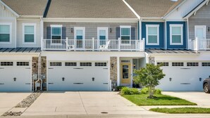 A row of townhouses with attached garages, a small front yard, and a clear sky.