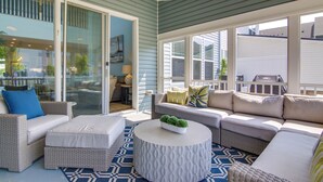 A covered patio area with wicker furniture, a round table with a plant, and a view of the outside.