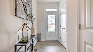 A hallway with a white door, a black console table with a glass terrarium, and a rustic wall art piece.