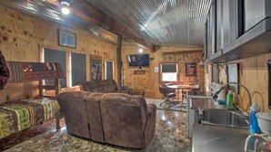 A cozy cabin interior with a sofa, a dining table, and a kitchen area with a sink and stove. - Pet-friendly Vacation Rental in Braymer! (Braymer)