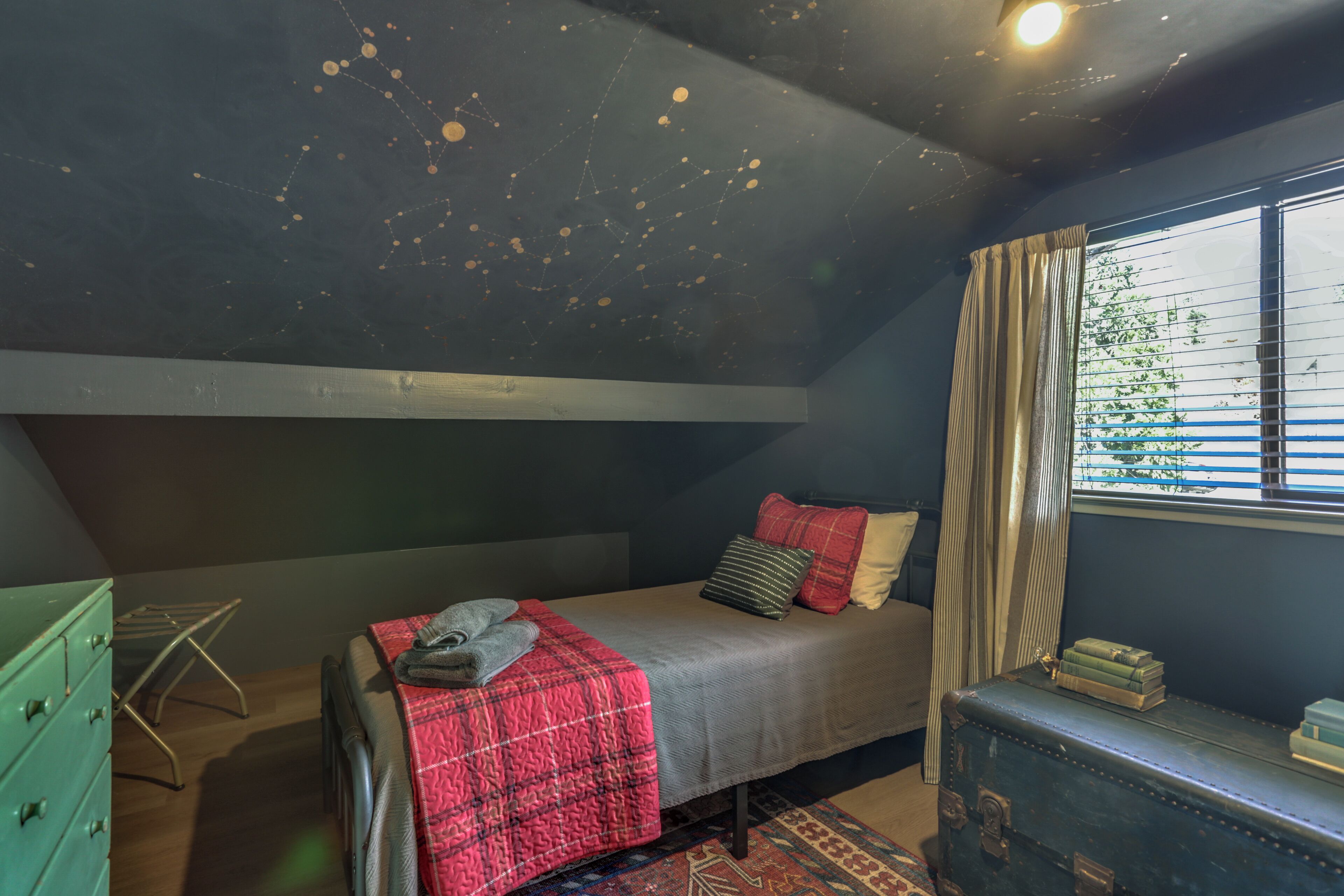 A bedroom with a bed, a dresser, a window with curtains, and a ceiling with a star-like design.