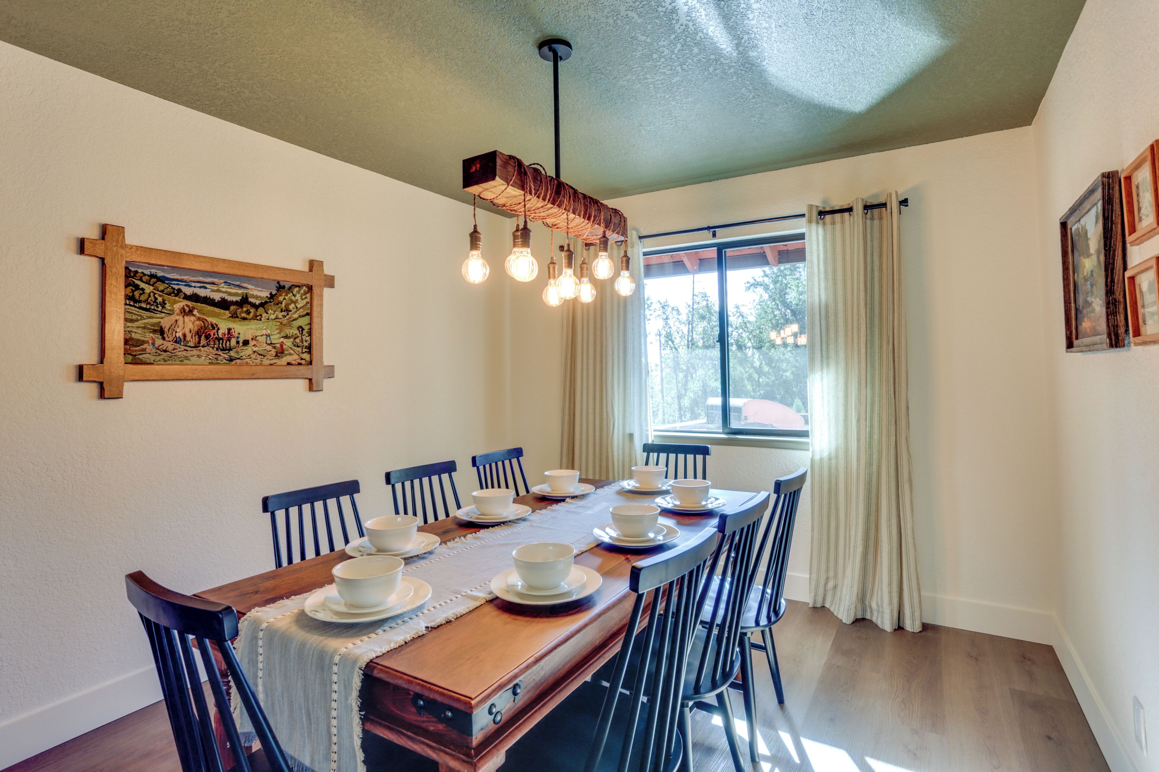 Un coin repas avec une table en bois dressée pour le repas, entourée de chaises, un tableau au mur et une fenêtre avec des rideaux.