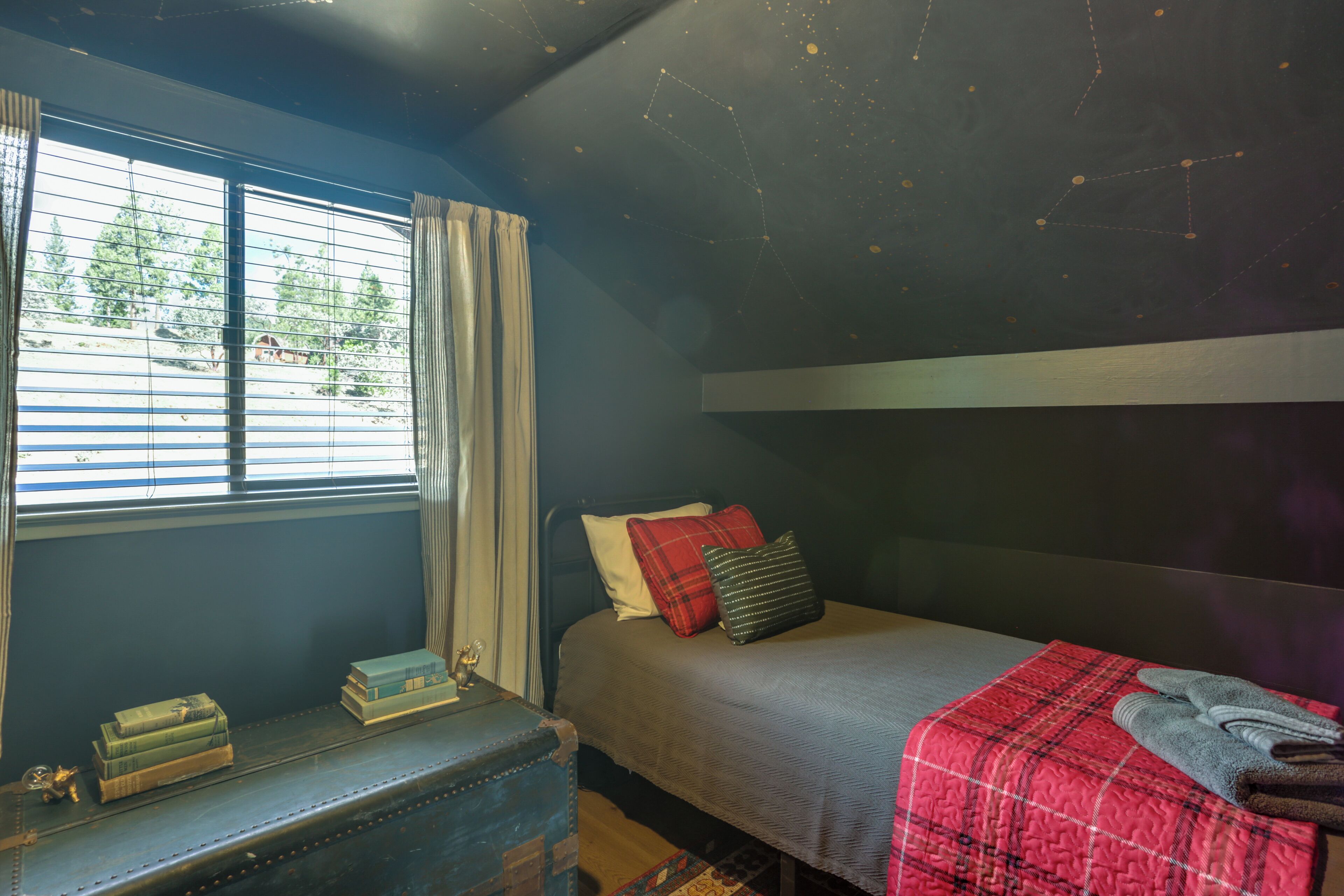 A bedroom with a bed, a window with curtains, a bedside table with books, and a starry ceiling design.