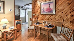 A wooden-paneled dining area with a table set for two, a chair, a lamp, and a framed picture on the wall.
