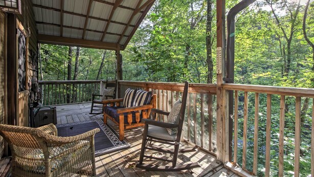 A wooden deck with a covered area, furnished with wicker chairs, a rocking chair, and a sofa.