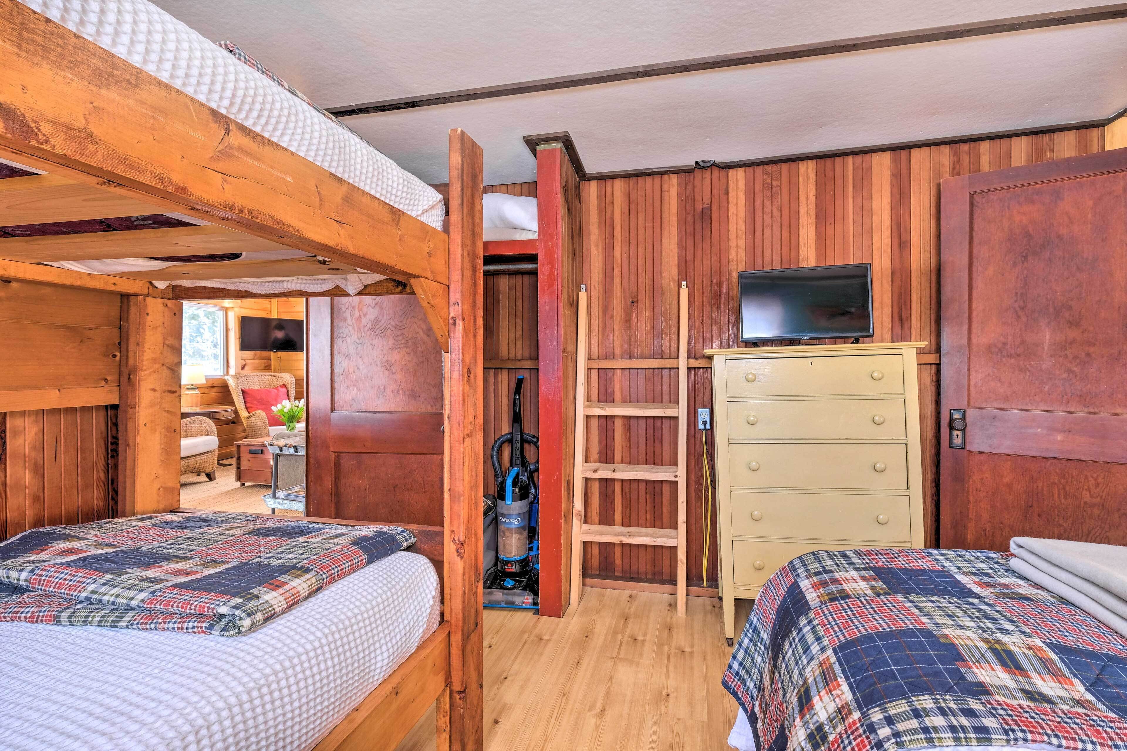 A room with two beds, a wooden wardrobe, a television, and a vacuum cleaner.