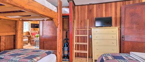 A room with two beds, a wooden wardrobe, a television, and a vacuum cleaner.