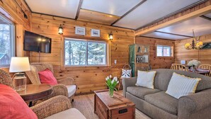 Ein gemütliches Blockhaus-Interieur mit Holzausstattung, einer Couch, einem Tisch mit Blumenvase und einem an der Wand montierten Fernseher.