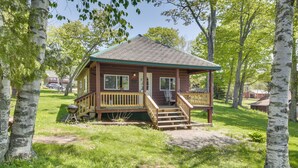 Eine Holzhütte mit Veranda und Stufen, umgeben von Bäumen und Gras.