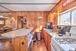 A wooden cabin kitchen with a central island, a stove, and a sink. - Picturesque Maine Getaway w/ Lake Access! (Rangeley)
