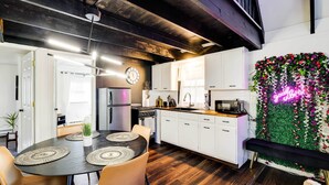 Eine moderne Küche mit weißen Schränken, einem Holztisch mit Tischsets und einem Neon-Leuchtschild an der Wand.