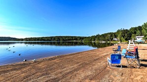 Ein Strand mit einer Reihe blauer und roter Liegestühle, einem weißen Rettungsschwimmerstand und einem ruhigen See mit Enten.