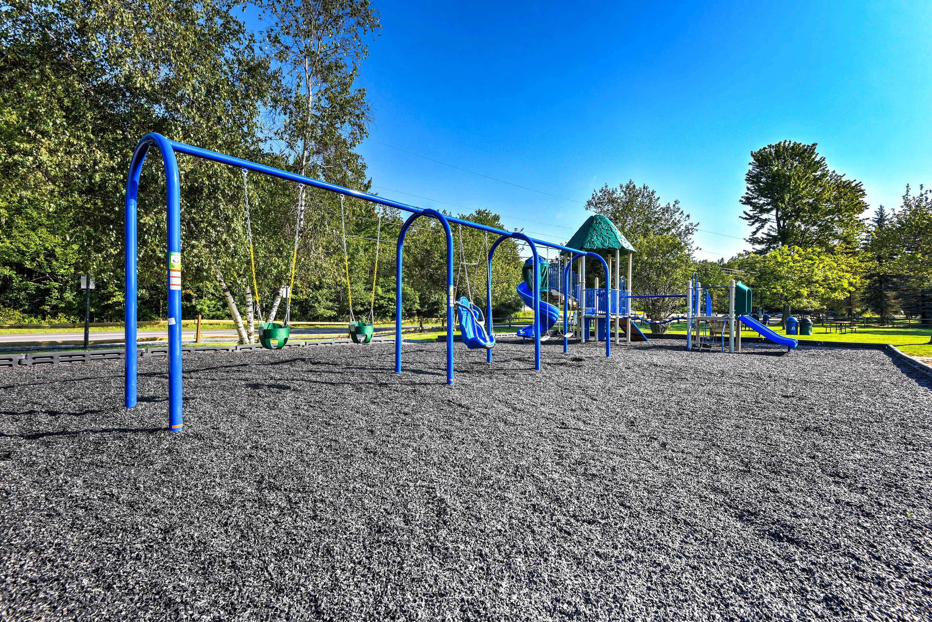 Un parque infantil con estructuras de juego azules y verdes, incluyendo toboganes y columpios, sobre una superficie de grava.