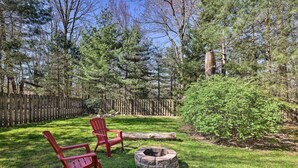 Ein Garten mit zwei roten Adirondack-Stühlen, einer Feuerstelle aus Stein und einem Holzzaun.