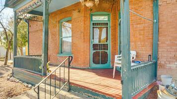 A porch with a green railing, a white chair, and a door with a window.