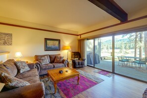 A living room with a sofa, armchairs, a coffee table, and a large sliding glass door leading to an outdoor area with a view of trees and a bench. - Quiet Unit w/ Golf Course & Mtn Views in Graeagle! (Blairsden-Graeagle)