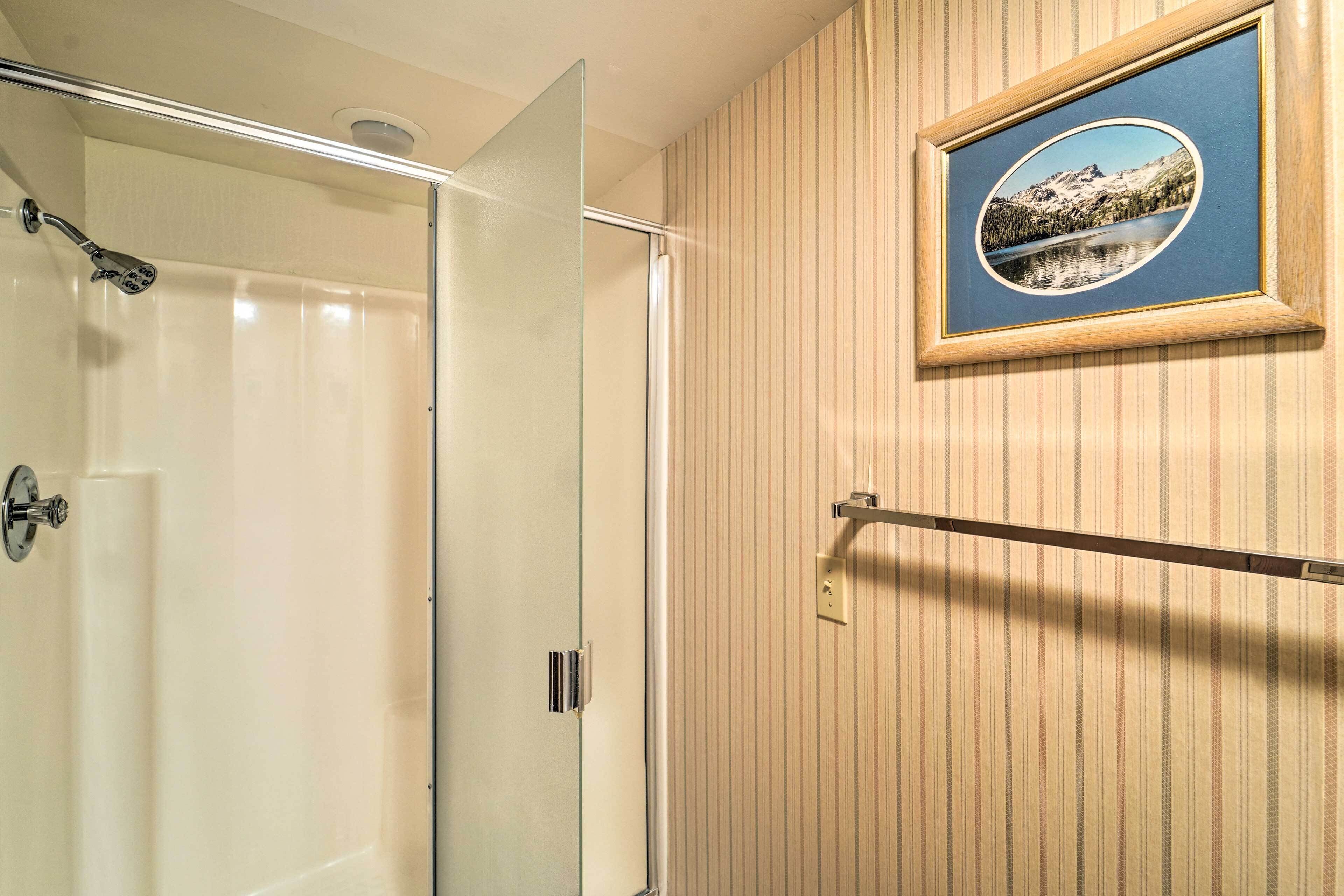 A bathroom with a glass shower enclosure, a wooden panel wall, and a framed picture of a mountain landscape.