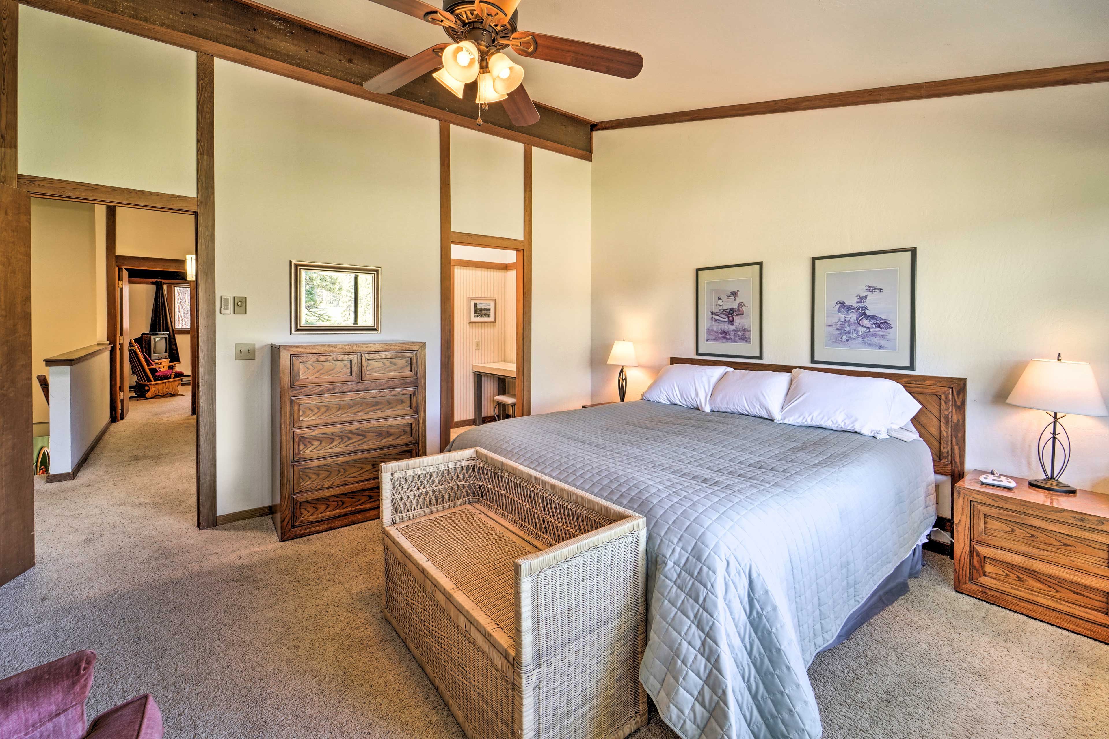 A bedroom with a large bed, wooden headboard, two bedside tables with lamps, a wicker side table, and a ceiling fan.