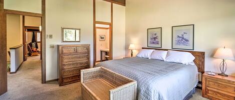 A bedroom with a large bed, wooden headboard, two bedside tables with lamps, a wicker side table, and a ceiling fan.