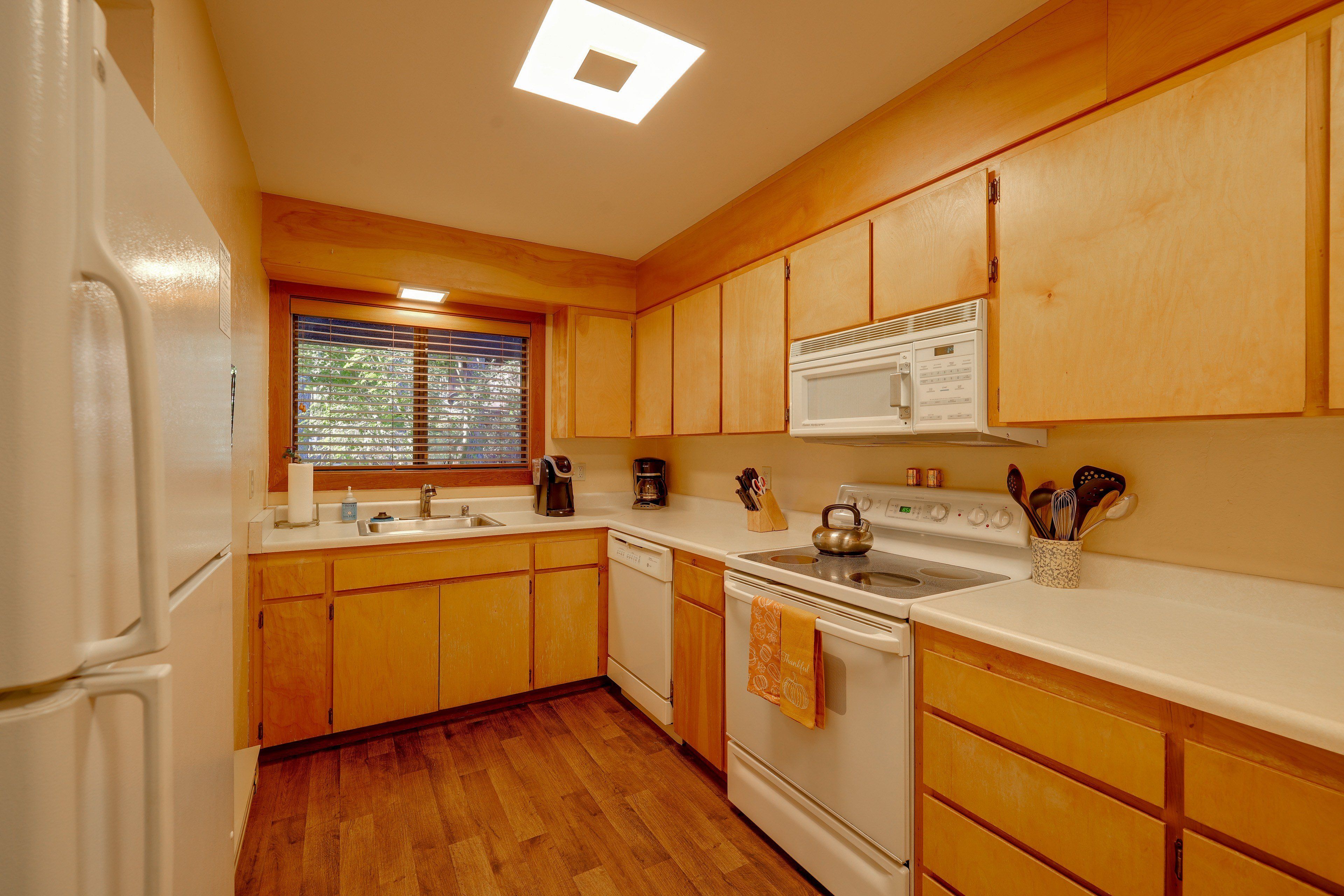 A kitchen with wooden cabinets, a stove, a microwave, and a window with blinds.