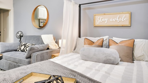 A modern bedroom with a bed, a grey sofa, a small table, and a mirror. - Relaxing Lubbock Studio ~ 6 Mi to Texas Tech (Lubbock)