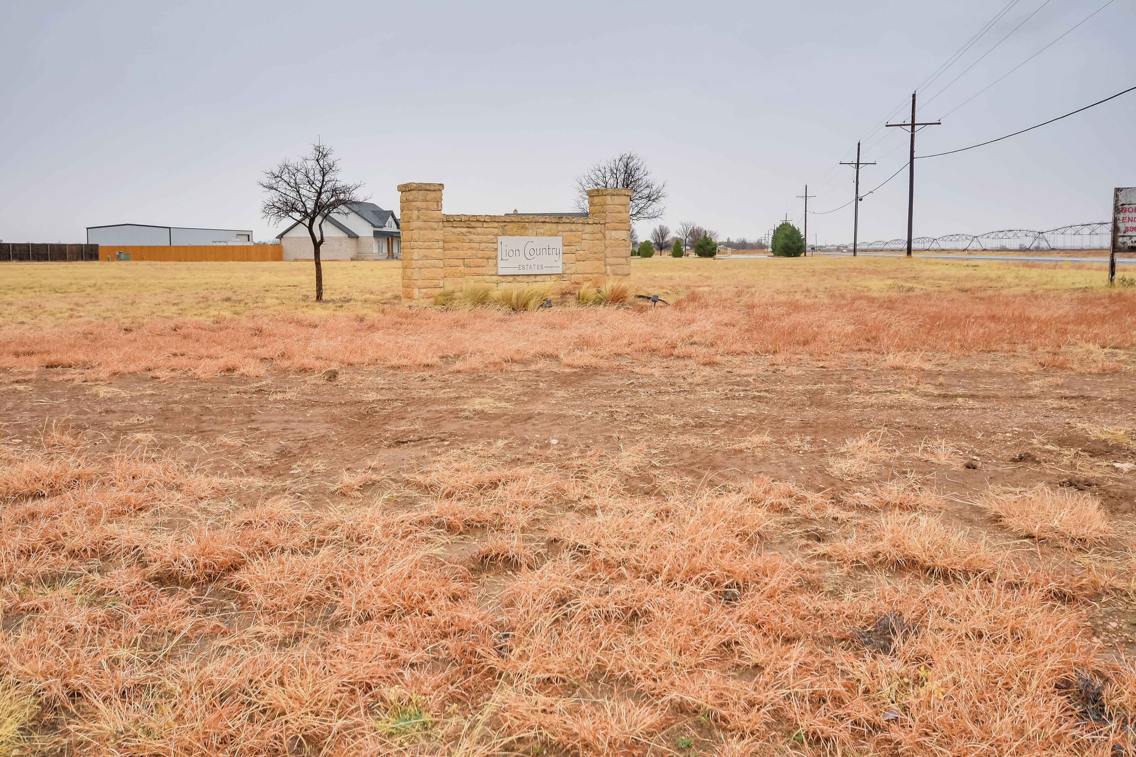 Señal de Lion Country Estates con un muro de piedra y un campo árido en primer plano.