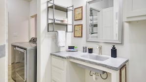 A modern bathroom with a built-in washing machine, a large mirror, and a granite countertop. - Relaxing Lubbock Studio ~ 6 Mi to Texas Tech (Lubbock)