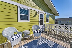 A porch with wicker chairs and a patterned rug, a white fence, and a green house. - Quaint 'sand Dollar Sandbar' - Walk to Beach! (Holly Ridge)
