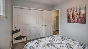 A bedroom with a bed, a ceiling fan, a door, a chair, and a painting on the wall.