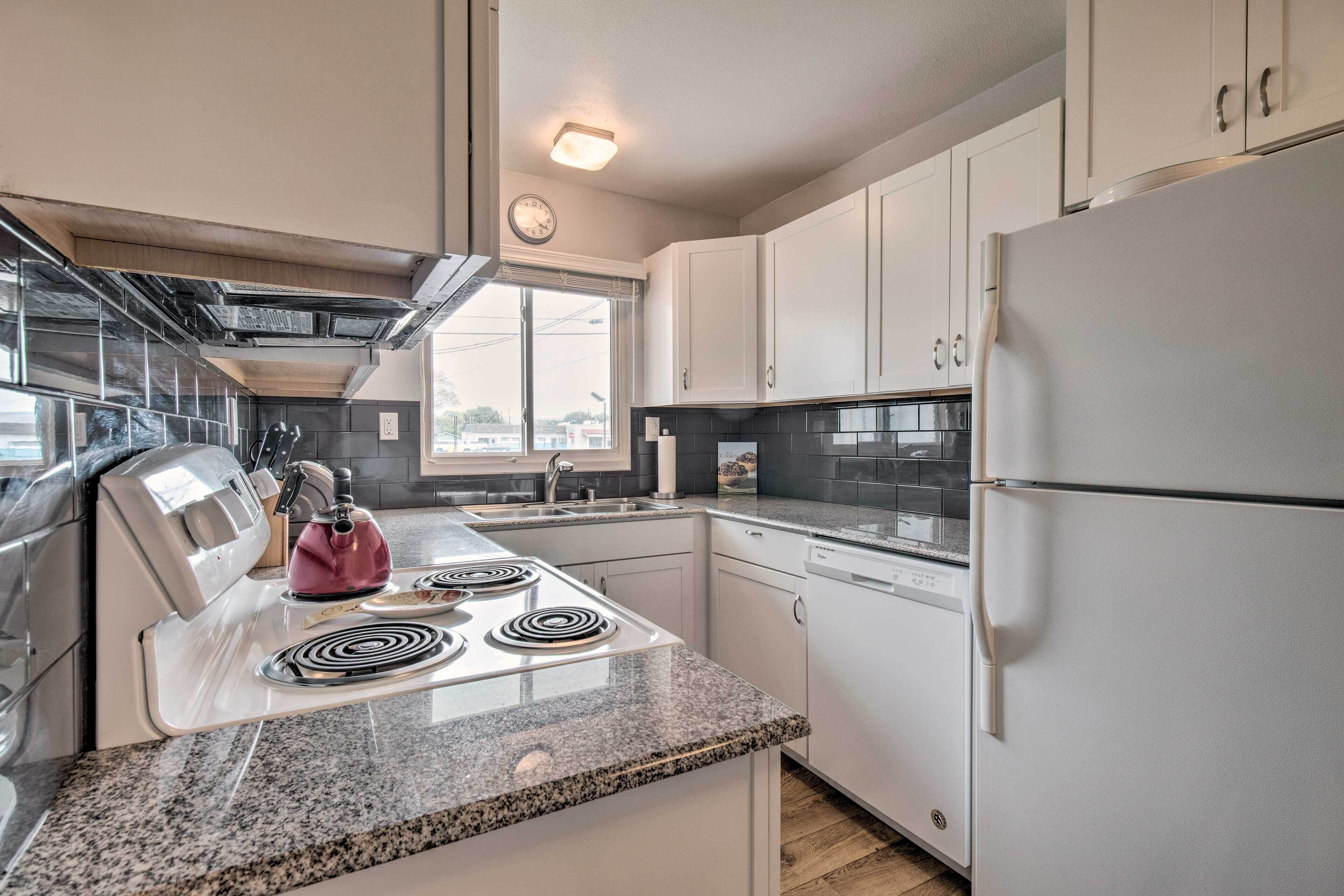 A modern kitchen with white cabinets, a stainless steel range hood, a built-in oven, a refrigerator, and a window providing natural light.