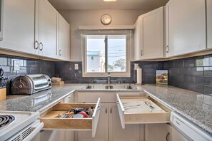 Una cocina moderna con armarios blancos, horno empotrado, tostadora y ventana con vistas al exterior.