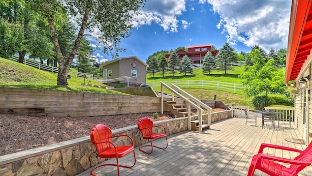 A wooden deck with red chairs, a stone retaining wall, and a view of a building with a clock. - Fish, Float & Relax Fireside: Home Near New River! (Crumpler)
