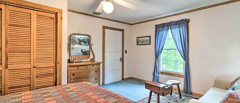A bedroom with a large bed, a ceiling fan, a dresser, a desk, and a window with curtains.