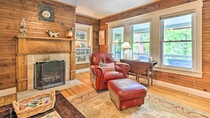 A cozy living room with a fireplace, leather armchair, ottoman, and large windows offering a view of the outdoors. - Fish, Float & Relax Fireside: Home Near New River! (Crumpler)