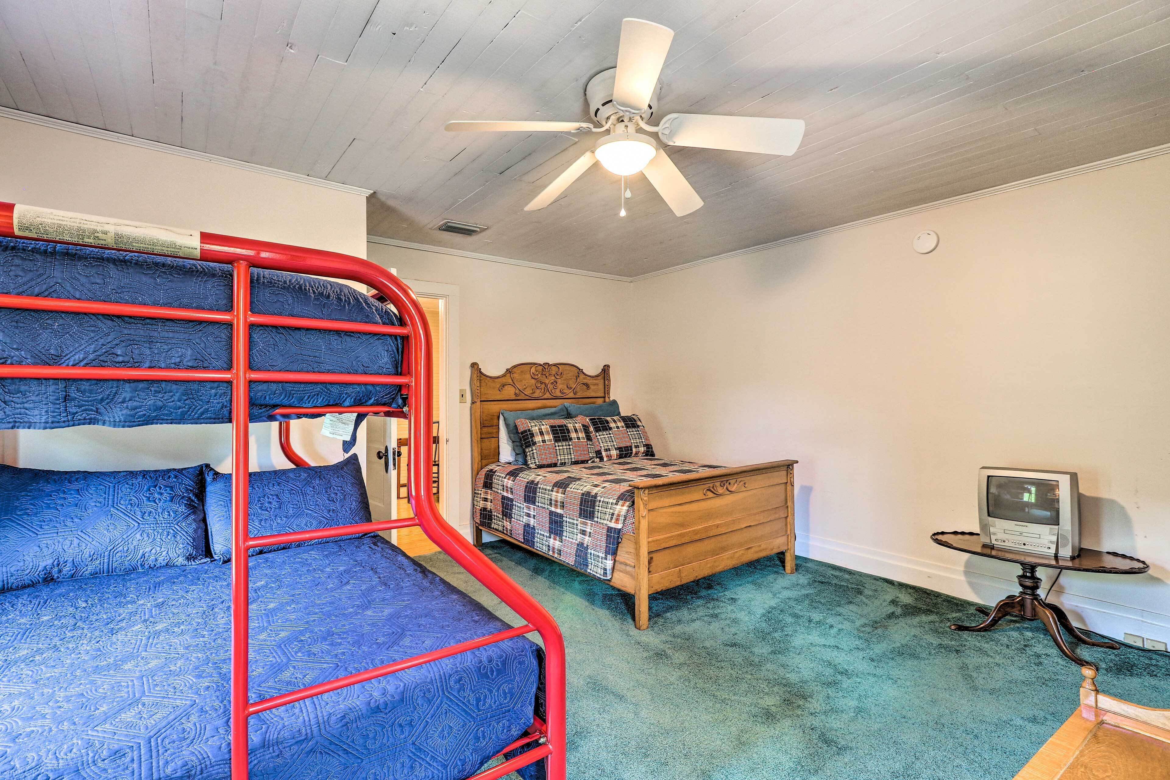A room with bunk beds, a wooden bed, a ceiling fan, a small table with a computer, and a carpeted floor.
