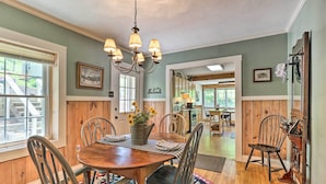 A dining area with a wooden table, chairs, and a chandelier. There is a window with blinds, a door leading to another room, and a rug on the floor. - Fish, Float & Relax Fireside: Home Near New River! (Crumpler)