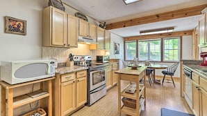 A kitchen with wooden cabinets, a microwave, stove, and a dining area with chairs and a table. - Fish, Float & Relax Fireside: Home Near New River! (Crumpler)