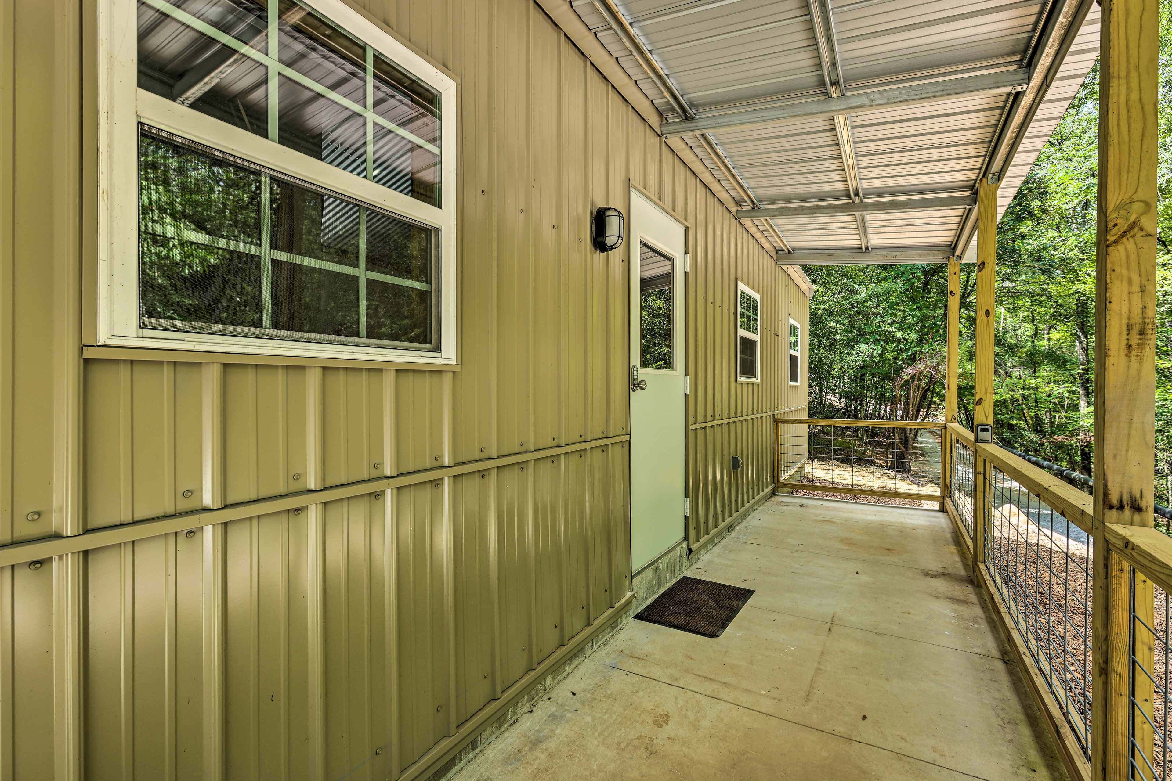 A covered porch with a metal roof, a wooden railing, and a concrete floor.