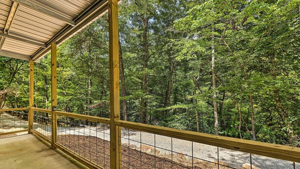 A covered outdoor area with a wooden railing, a gravel path, and a forested background. - Quaint Tallassee Cabin: Stone Creek On-site! (Tallassee)