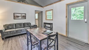 A room with a wooden dining table, black chairs, a gray sofa, a framed picture on the wall, and a door with a window. - Quaint Tallassee Cabin: Stone Creek On-site! (Tallassee)