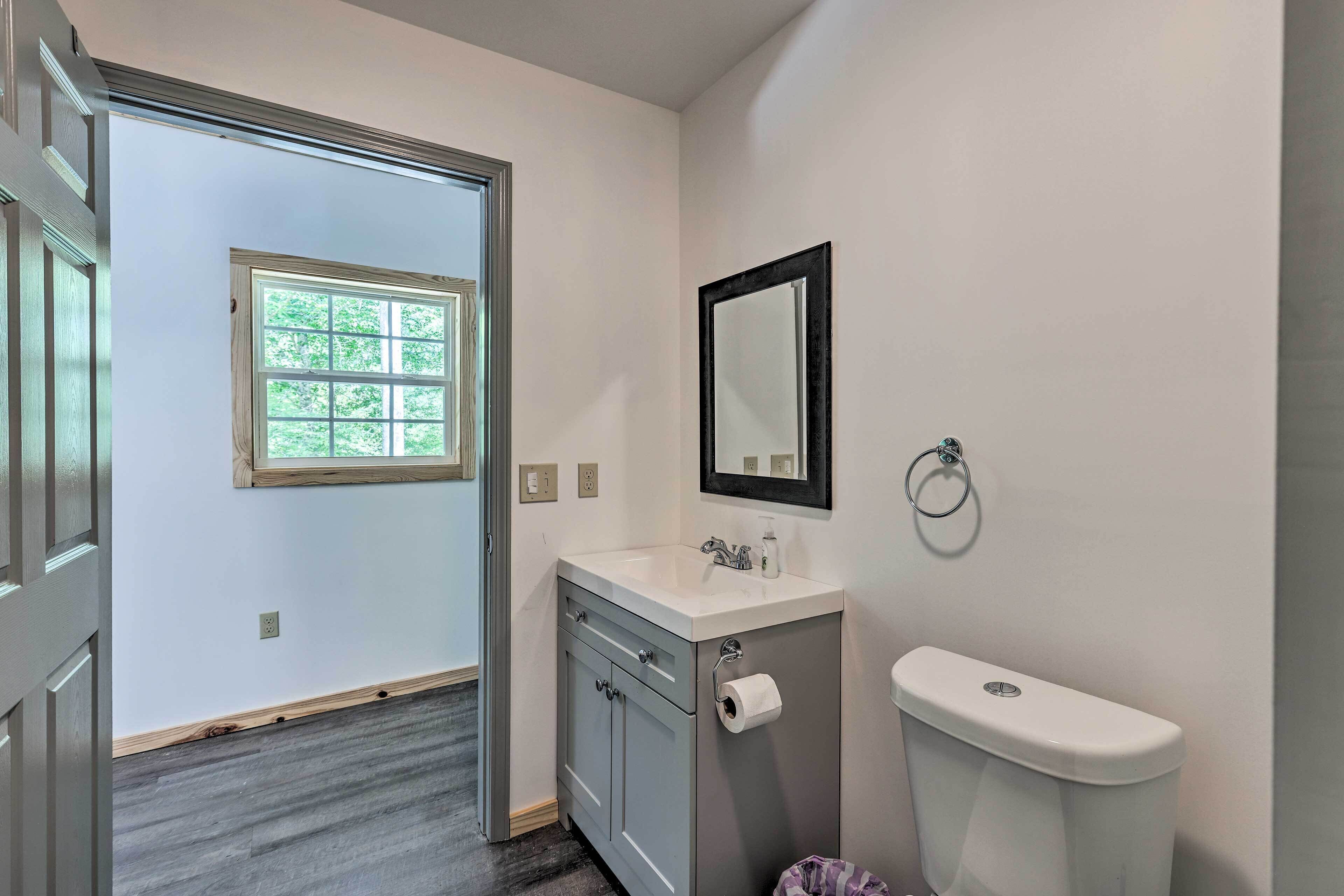 A bathroom with a window, a sink, a toilet, and a mirror.