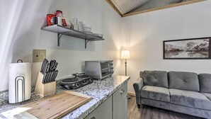 A compact kitchen with a countertop, toaster, and a cutting board. There is a sofa and a painting in the living area. - Quaint Tallassee Cabin: Stone Creek On-site! (Tallassee)