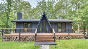 A modern house with a stone foundation, a wooden deck, and a glass door. - Pocono Lake Cabin w/ Hot Tub & Resort Amenities! (Pocono Lake)