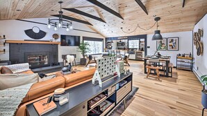 A spacious living area with a fireplace, leather sofa, wooden dining table, and a kitchen in the background. - Pocono Lake Cabin w/ Hot Tub & Resort Amenities! (Pocono Lake)