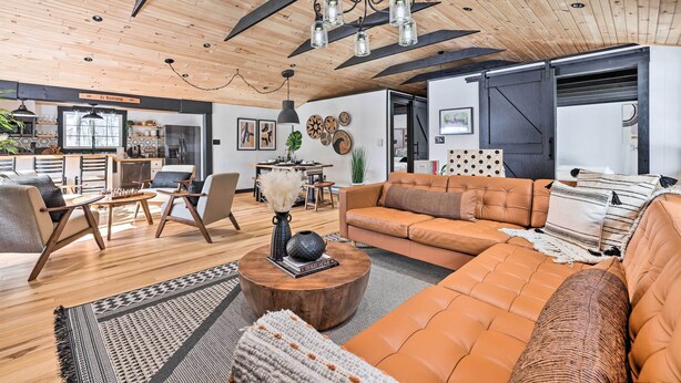 A modern living room with a wooden ceiling, a large sofa, a coffee table, and a chandelier. - Pocono Lake Cabin w/ Hot Tub & Resort Amenities! (Pocono Lake)