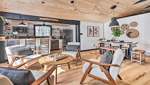 A modern living room with wooden flooring, a dining area, and a kitchen visible through an open door. - Pocono Lake Cabin w/ Hot Tub & Resort Amenities! (Pocono Lake)
