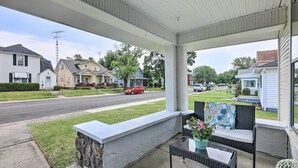 A covered porch with a stone bench, a table with a vase of flowers, and a view of a residential street.