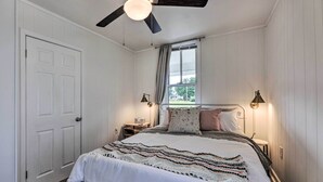 A bedroom with a bed, a ceiling fan, a window with curtains, bedside lamps, and a door.