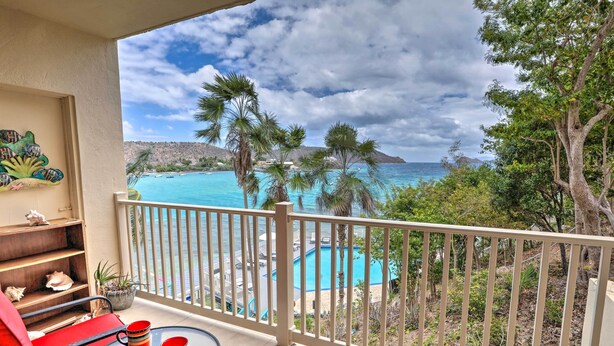 A balcony with a view of a turquoise pool, red chairs, and a tropical landscape. - Saint Thomas Condo w/ Ocean Views, Walk to Beach! (St. Thomas)